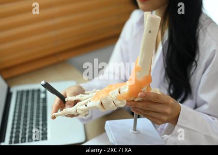 Medico ortopedico professionista che spiega al paziente il trattamento, indicando il modello di caviglia e ossa del piede Foto Stock