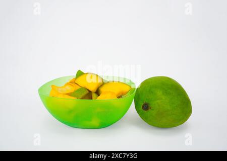 Fette di mango in una ciotola verde con un mango, isolate su sfondo bianco Foto Stock