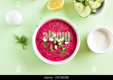 Zuppa di barbabietole estive fredda fatta in casa in un recipiente bianco su sfondo verde. Disintossicazione sana o concetto di cibo vegetariano. Vista dall'alto, disposizione piatta Foto Stock