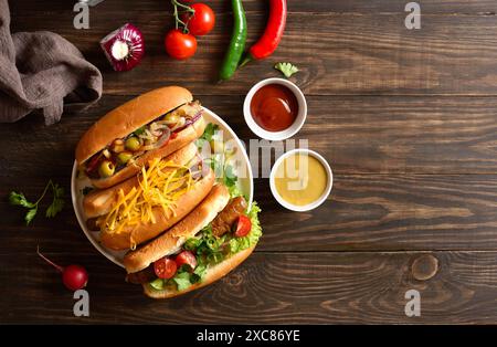 Hot dog con diverse guarnizioni su piatto bianco su fondo in legno con spazio libero. Vista dall'alto, disposizione piatta Foto Stock