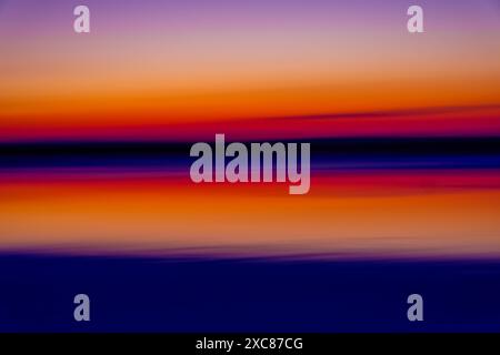 Splendida immagine astratta di un tramonto sull'oceano, che mostra vivaci sfumature di arancione, rosso e viola in un paesaggio etereo e sfocato. Foto Stock