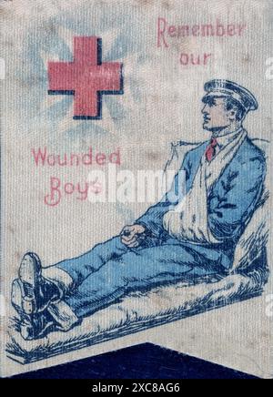 Un distintivo di seta della prima guerra mondiale, stampato in rosso e blu su sfondo bianco. Il distintivo presenta un soldato reclinato in uniforme da ospedale, con il braccio in una fionda. Il soldato indossa un berretto ed è vestito con pantaloni blu e una camicia bianca. Una croce rossa e una croce maltese dell'ambulanza di St Johns sono sovrapposte nell'angolo in alto a sinistra, circondate dall'iscrizione rossa che ricorda i nostri ragazzi feriti. Foto Stock