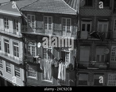 una vecchia donna sta appendendo il suo bucato appena lavato e i vestiti fuori dal suo balcone. Facciata dell'edificio in bianco e nero. Porto.Portugal 29.05.2024 Foto Stock