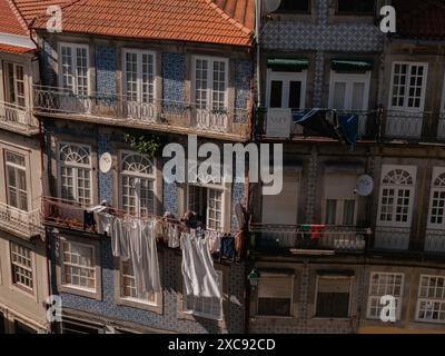 una vecchia donna sta appendendo il suo bucato appena lavato e i vestiti fuori dal suo balcone. Facciata colorata dell'edificio. Porto. Portogallo 29.05.2024 Foto Stock