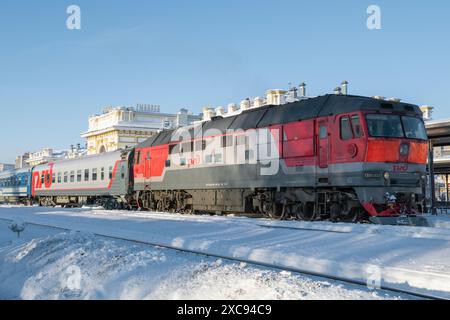 RYBINSK, RUSSIA - 3 GENNAIO 2024: Locomotiva diesel russa TEP70 con un treno passeggeri sulla stazione di Rybinsk in un giorno di sole gennaio Foto Stock