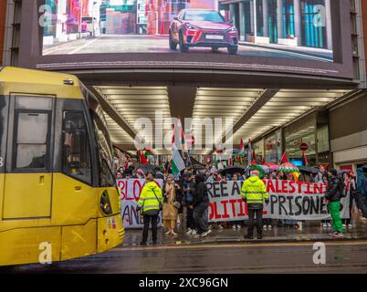 Manchester, Regno Unito. 15 giugno 2024. Il Manchester tram passa davanti alle proteste di guerra di Gaza in Palestina a Manchester nel Regno Unito durante le forti piogge. I manifestanti hanno marciato da Piazza San Pietro attraverso il centro della città. Gli striscioni includevano messaggi che chiedevano a Israele di liberare i prigionieri politici palestinesi e criticavano la Barclays Bank. Crediti: GaryRobertsphotography/Alamy Live News Foto Stock