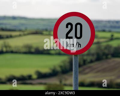 Un segnale rosso e bianco del limite di velocità di 20 km/h si trova su uno sfondo verde sfocato, a indicare una regolamentazione del traffico in un'area verdeggiante. Foto Stock