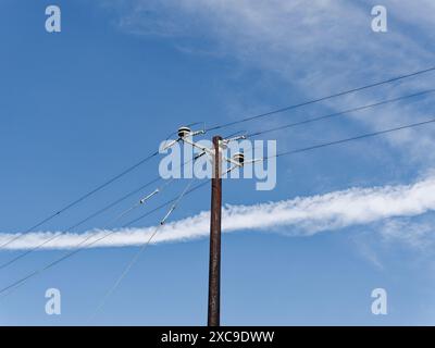 Un vecchio polo di alimentazione con linee contro un cielo blu con nuvole che simboleggiano una connettività duratura. Foto Stock