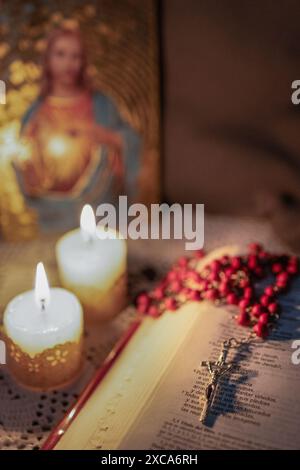 Rosario rosso sulla Bibbia, illuminato dalla luce delle candele. Sfondo sfocato Foto Stock