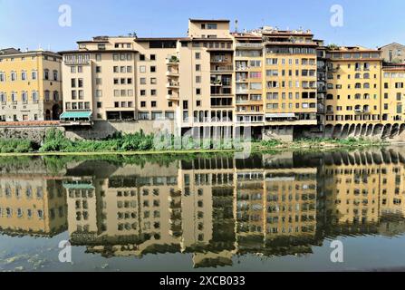 Diverse file di case si trovano lungo un fiume, (Arno) i loro riflessi possono essere visti nell'acqua, in una giornata limpida, Firenze, Toscana, Italia Foto Stock