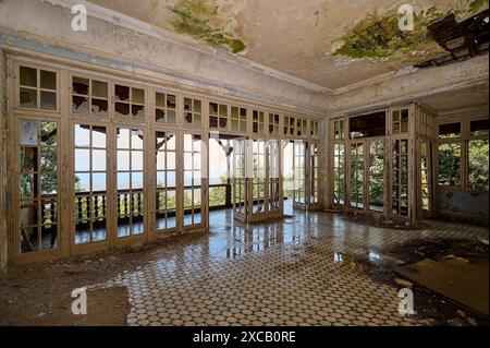 Camera abbandonata con finestre rotte, pavimento fatiscente e vista sul verde della natura, Villa Mussolini, Villa de vecchi, Profitis Ilias, Empona, Rodi Foto Stock