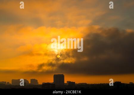 Alba. Il sole attraversa le nuvole nel cielo mattutino sopra la città. Sagome di edifici in controluce Foto Stock
