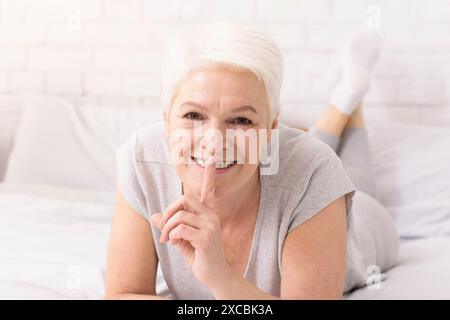 Donna anziana con capelli bianchi che posiziona le dita sulle labbra Foto Stock
