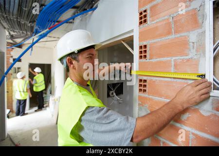 Lavoratore con attrezzature di protezione, PPE, tenendo il nastro retrattile misure, la costruzione di alloggi, muro di mattoni, Paesi Baschi Foto Stock