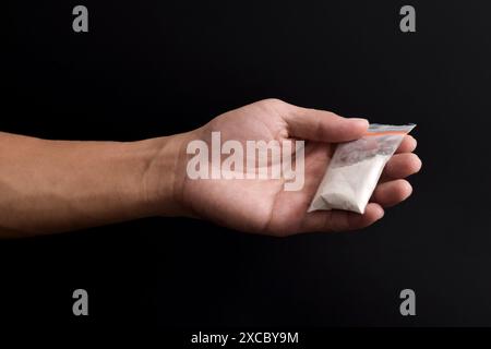 Cocaina a mano in un contenitore di plastica isolato su sfondo nero. Illustrazione di sostanze stupefacenti illegali, narcotici Foto Stock