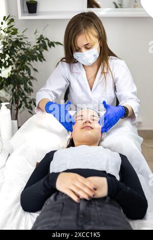 Un cosmetologo esperto, estetista esegue un massaggio facciale rilassante per il cliente per preparare la pelle ad una procedura cosmetica, promuovendo Foto Stock