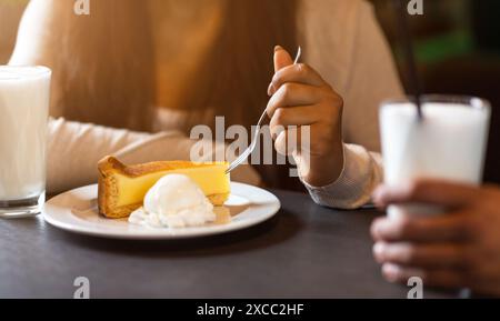 Ragazza che si gusta Cheesecake e Milkshake all'accogliente Cafe in serata Foto Stock