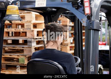 Operaio di magazzino che gestisce un carrello elevatore, movimenta pallet in legno per la gestione dell'inventario e la logistica. Foto Stock