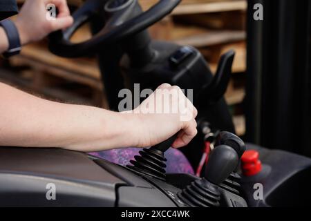 Primo piano della mano di una persona che aziona i comandi di un carrello elevatore a forche in un ambiente industriale. Foto Stock