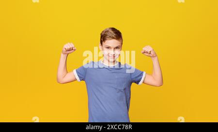 Ragazzo carino che mostra bicipite su sfondo arancione Foto Stock