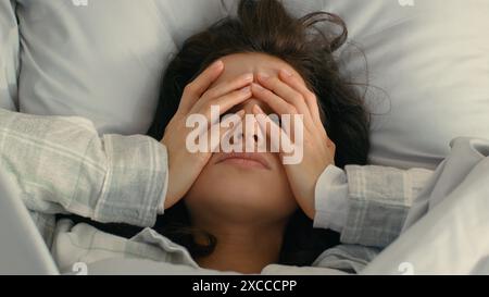 Primo piano la giovane donna caucasica toccando il viso la testa le mani mal di testa emicrania sensazione di malattia espressione esausta femmina a letto malstanche Foto Stock