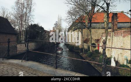 Un tranquillo canale a Bruges, con una barca piena di turisti che gode della vista panoramica degli storici edifici in mattoni e dei canali alberati. Foto Stock