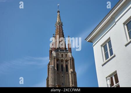 Bruges, Belgio; giugno 06.2024; la torre della chiesa di nostra Signora in stile gotico con vecchie case con frontoni a punta al sole come parte dell'UNESCO W Foto Stock