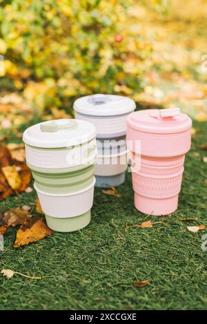 Tazze pieghevoli ecologiche o tazze pieghevoli in silicone con erba verde e foglie cadute sullo sfondo autunnale Foto Stock