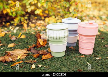 Tazze pieghevoli ecologiche o tazze pieghevoli in silicone con erba verde e foglie cadute sullo sfondo autunnale Foto Stock