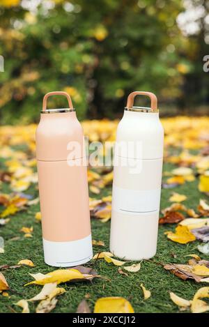 Moderno termos in acciaio inox e plastica con tazza in parco in autunno. termos sottovuoto. Concetto per attività all'aperto, bevande calde, escursioni, viaggi. Foto Stock