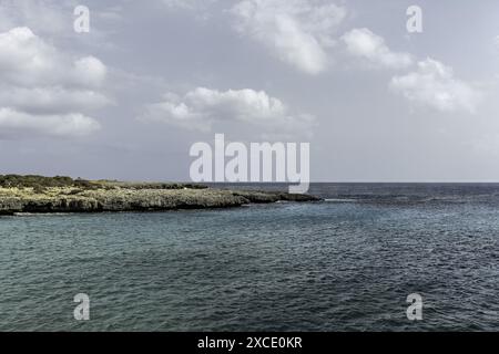 Visitatori che si godono una giornata di sole sulla spiaggia di Cala en Bosch a Minorca. La spiaggia sabbiosa, le acque calme e il cielo parzialmente nuvoloso creano un ambiente ideale per rilassarsi Foto Stock