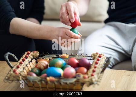 spillatura delle uova di pasqua, spillatura delle uova di mamma e figlio accanto al cestino con uova di pasqua, messa a fuoco selettiva, primo piano delle mani che toccano le uova Foto Stock