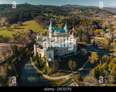 Vista panoramica aerea di Bojnicky Zamok, castello medievale di Bojnice, Slovacchia. Vista dall'alto della famosa fortezza in pietra e della foresta all'orizzonte, con paesaggi con edifici storici sulla collina con fossato Foto Stock