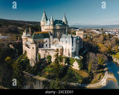 Vista aerea del castello di Bojnice in Slovacchia. Alto scenario panoramico del Bojnicky Zamok medievale sotto il cielo blu, muri in pietra della fortezza con piante verdi e pini, fossato con acqua e collina Foto Stock