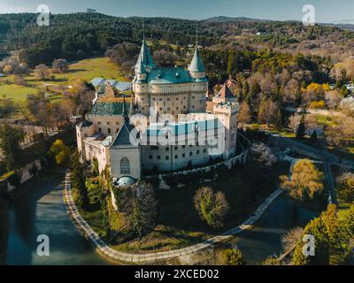 Vista panoramica aerea del castello di Bojnice in Slovacchia. Paesaggio panoramico con il famoso palazzo e la storica fortezza patrimonio dell'UNESCO tra alberi di parco, strada e fossato profondo con acqua Foto Stock