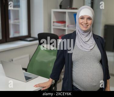 Donna caucasica incinta in hijab che lavora in ufficio. Foto Stock
