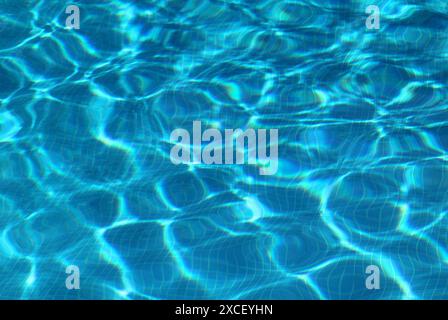 Concetto: Estate, tempo libero, stile di vita. Superficie della piscina con motivi a ondulazione e riflessi leggeri. Pavimento piastrellato in ceramica blu. Foto Stock