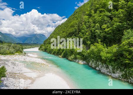 Una pittoresca scena di un fiume turchese che si snoda attraverso una lussureggiante valle verde, con torreggianti montagne sullo sfondo e un cielo blu punteggiato di influenza Foto Stock