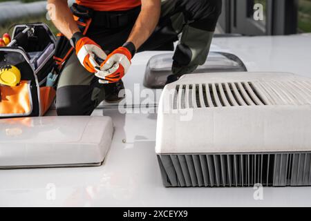 Un tecnico che indossa i guanti sta lavorando sul condizionatore d'aria di un RV. Il condizionatore d'aria è bianco con griglia grigia. Il tecnico indossa Foto Stock