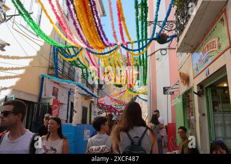 Persone che camminano per le strade di Alfama durante i popolari festeggiamenti dei Santi a Lisbona, in Portogallo, con tipiche decorazioni colorate di strada Foto Stock