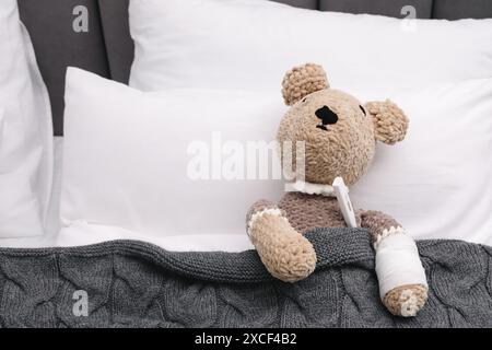 Simpatico orsacchiotto con bendatura e termometro sotto coperta nel letto Foto Stock