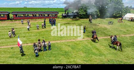 Ronks, Pennsylvania, USA, 8 giugno 2024 - persone nelle uniformi della Guerra civile in piedi su Un campo erboso accanto a Una locomotiva fumante, impegnata in Una rievocazione, con cavalli, tende, Un cannone e Una bandiera storica sotto cieli azzurri. Foto Stock