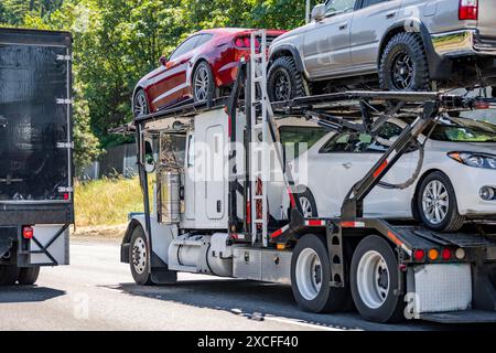 Trattore semi-camion per trasporto di autovetture bianche con cabina corazzata alimentata da trasporto industriale che trasporta autovetture e incroci su semi-traile rosso a due livelli idraulico Foto Stock