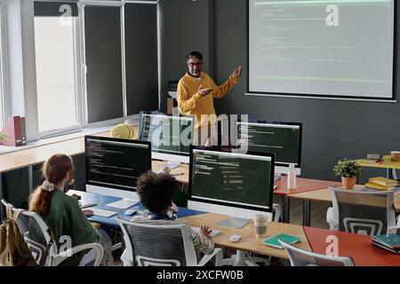 Insegnante birazziale maturo di informatica che spiega soggetto a gruppo di adolescenti durante la lezione a scuola Foto Stock