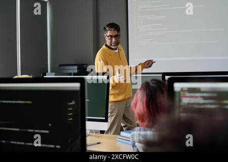 Insegnante moderno e maturo di informatica che si trova di fronte agli studenti in classe moderna e che conduce lezioni Foto Stock