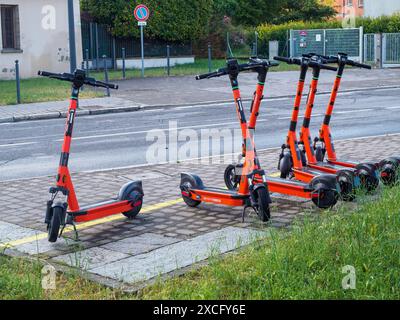 Cremona, Italia - 10 giugno 2024 sul marciapiede sono allineati diversi scooter elettrici in arancione, disponibili per il noleggio Foto Stock