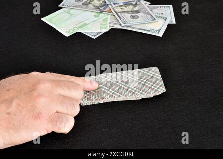 L'immagine mostra la mano del giocatore su un mazzo di carte e un mucchio di soldi a lato. Foto Stock