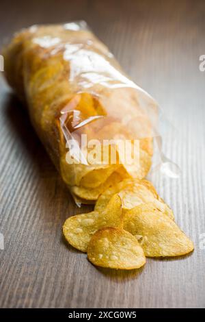 Patatine croccanti versate da un sacchetto di plastica su un tavolo di legno Foto Stock