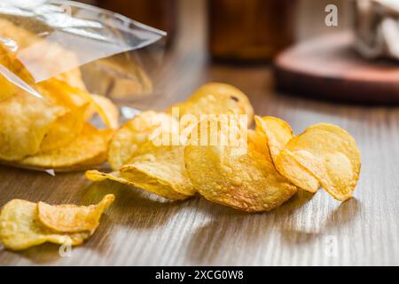 Patatine croccanti versate da un sacchetto di plastica su un tavolo di legno Foto Stock