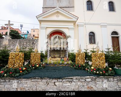 Culla di Natale e corona d'Avvento sulla piazza della chiesa, Chiesa della Natività della Vergine Maria, Mali Losinj, Croazia Foto Stock